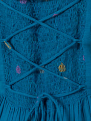 Teal cotton maxi dress with smocked texture and colorful polka dot embroidery, close-up back view showing crisscross straps and tie detail