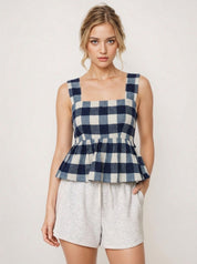Woman wearing a blue and white checkered top with gray shorts on a plain background