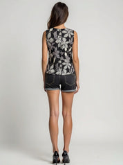 Woman wearing a sleeveless floral top and denim shorts on a plain background