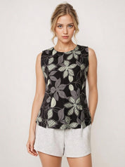 Woman wearing a sleeveless black floral top and white shorts on a light background