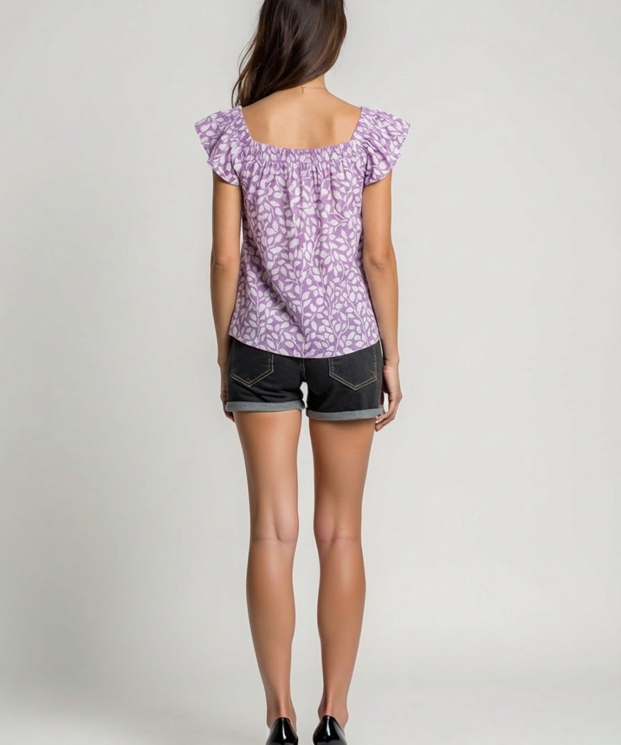 Woman wearing a purple floral top and black shorts on a plain background