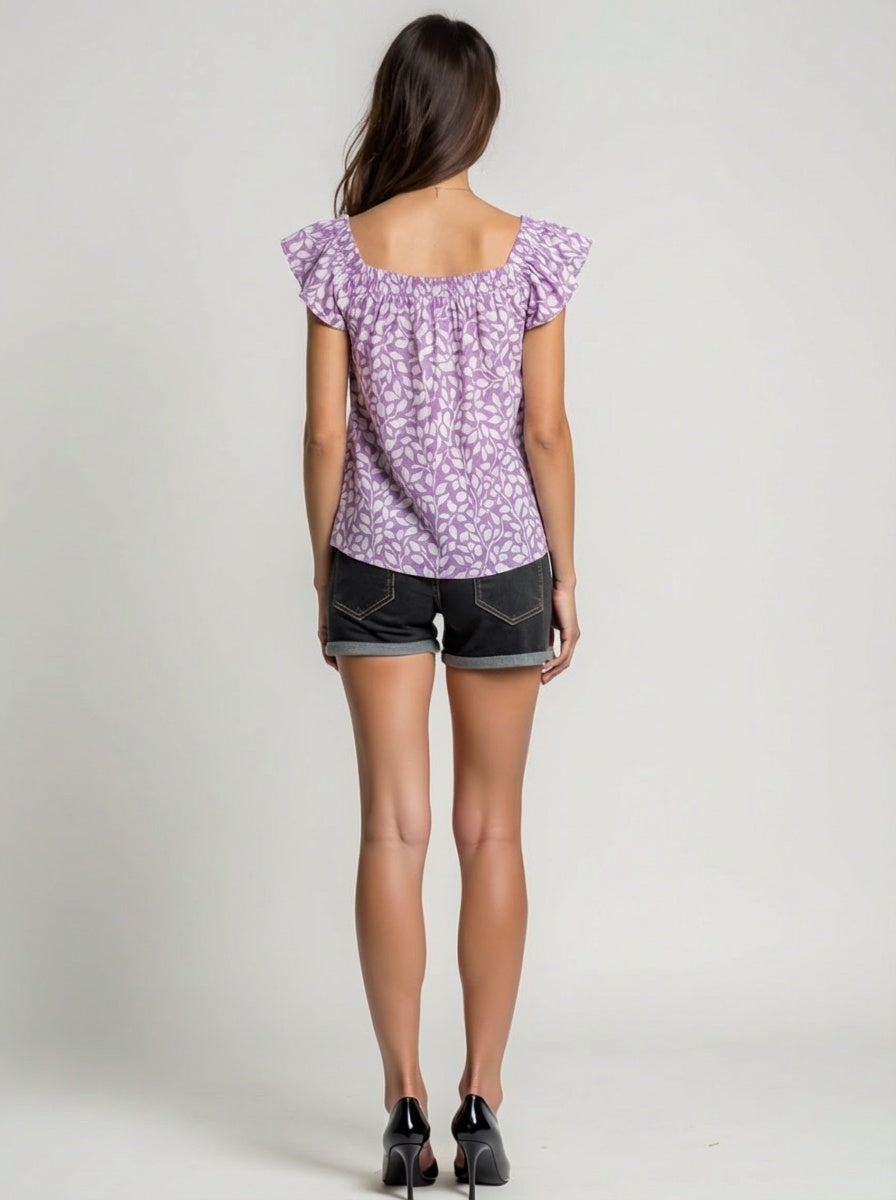 Woman wearing a purple floral top and black shorts on a plain background