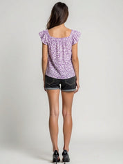 Woman wearing a purple floral top and black shorts on a plain background