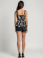 Woman wearing a patterned sleeveless top and denim shorts on a plain background