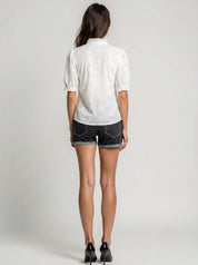 Person wearing a white patterned shirt and black shorts on a plain background