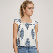 Woman wearing a white top with blue leaf patterns and blue jeans on a light background