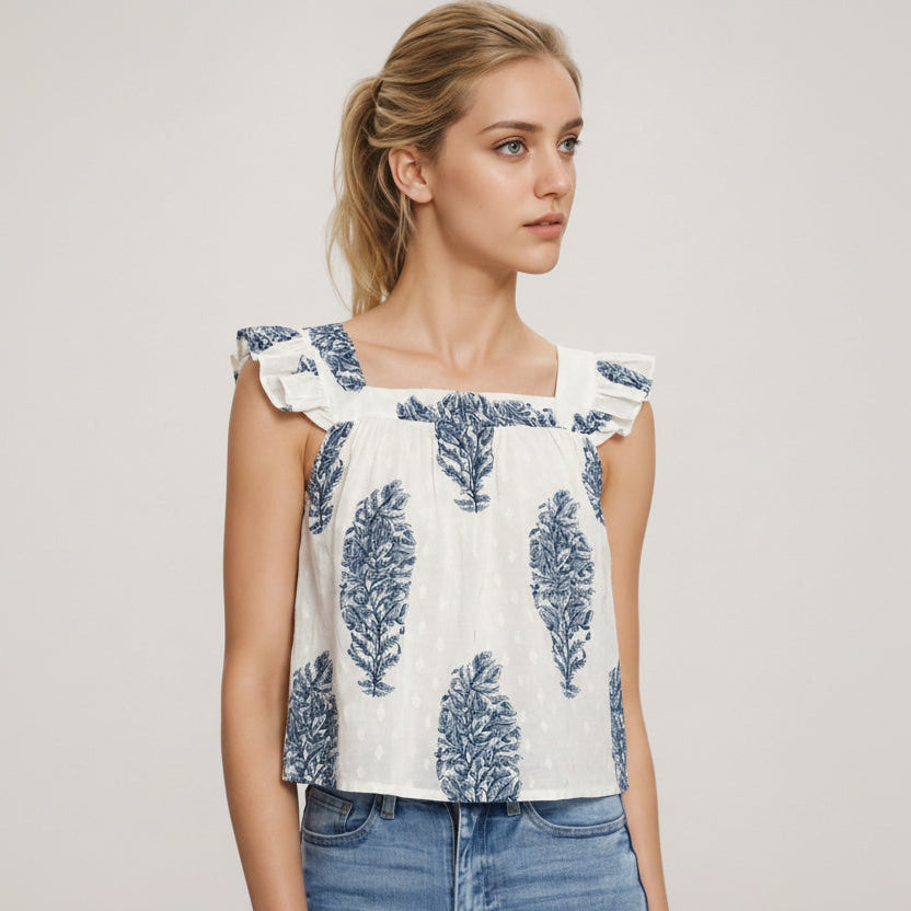 Woman wearing a white top with blue leaf patterns and blue jeans on a light background