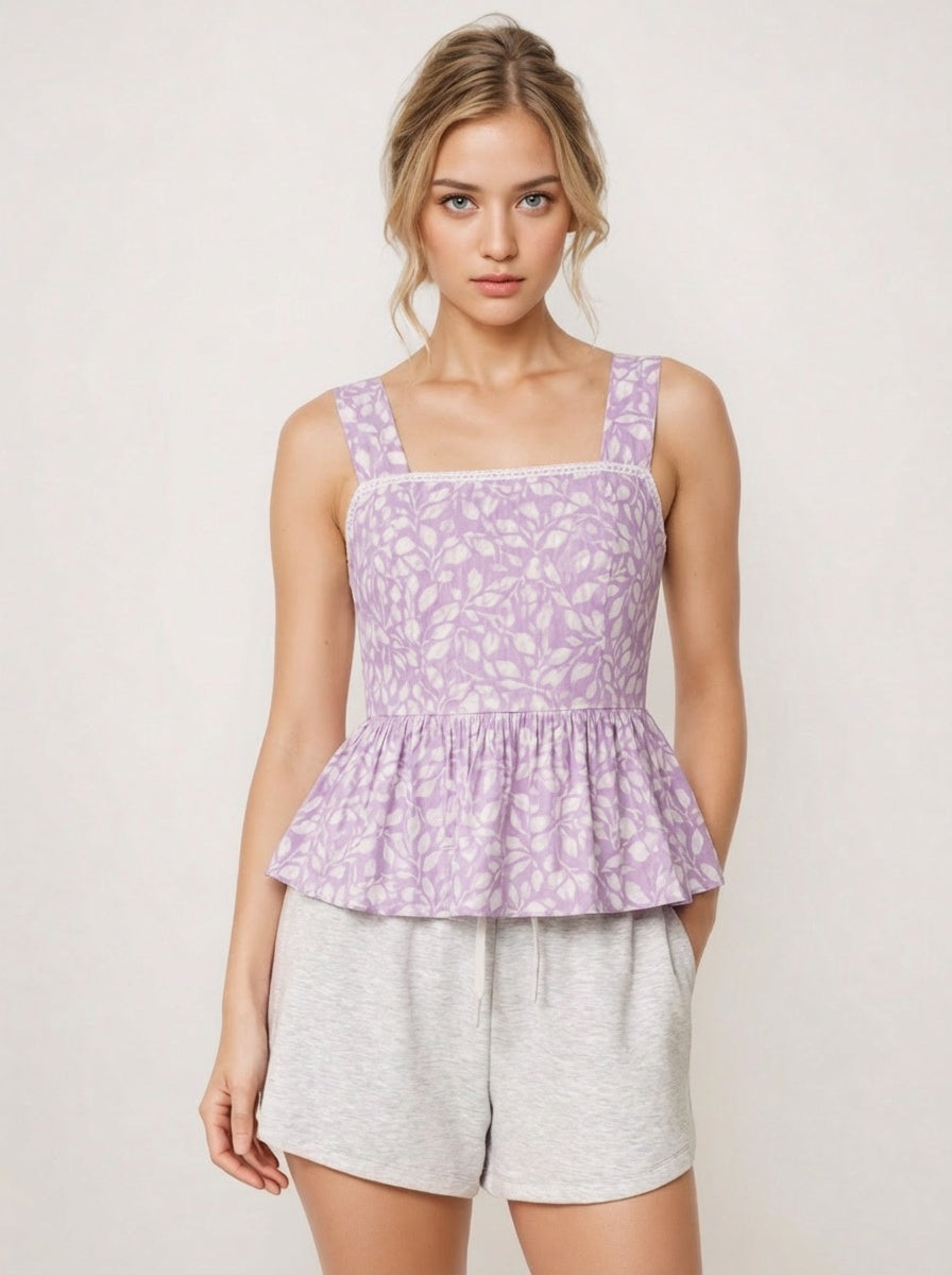 Woman wearing a purple floral peplum top and gray shorts on a white background