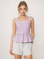 Woman wearing a purple floral peplum top and gray shorts on a white background