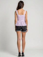 Woman wearing a purple peplum top and black shorts on a plain background