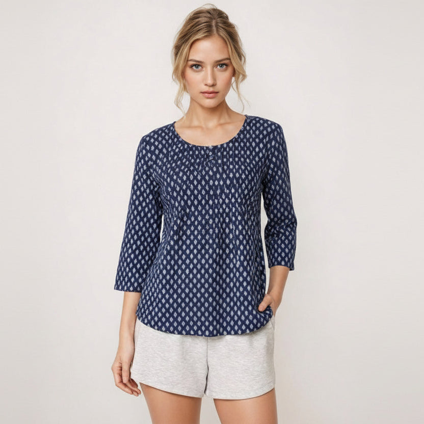 Woman wearing a blue patterned top and white shorts on a light background
