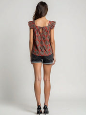 Woman wearing a patterned top and denim shorts on a plain background
