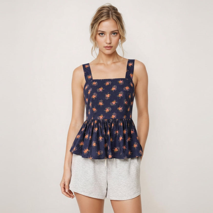Woman wearing a navy floral peplum top and light gray shorts on a white background