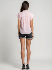 Person wearing a pink short-sleeve shirt and black shorts on a plain background