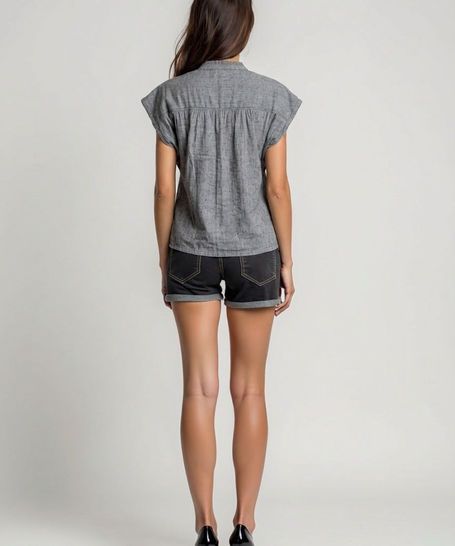 Woman wearing a gray short-sleeve shirt and denim shorts on a plain background