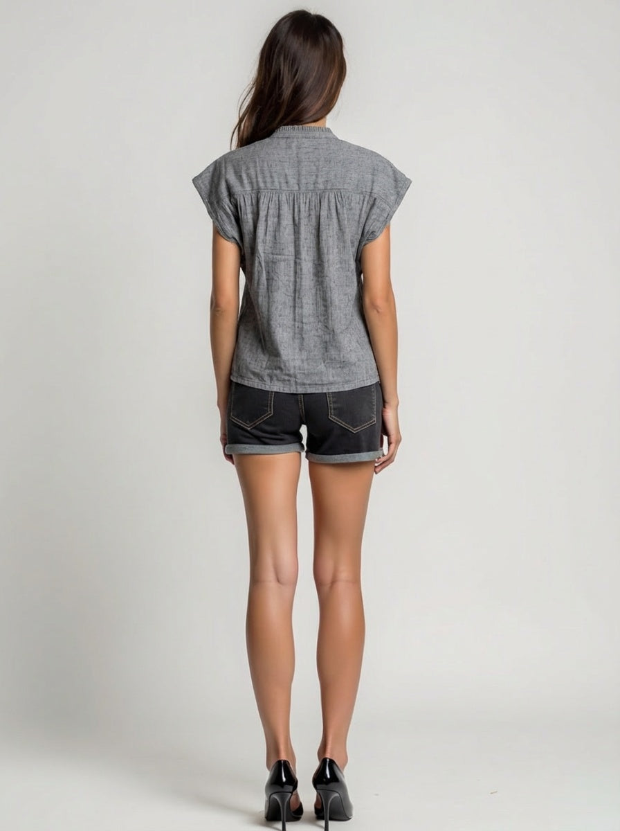 Woman wearing a gray short-sleeve shirt and denim shorts on a plain background
