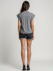 Woman wearing a gray short-sleeve shirt and denim shorts on a plain background