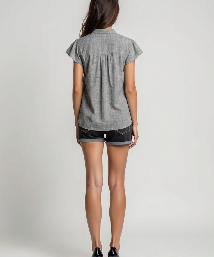 Woman wearing a gray short-sleeve shirt and black shorts on a plain background