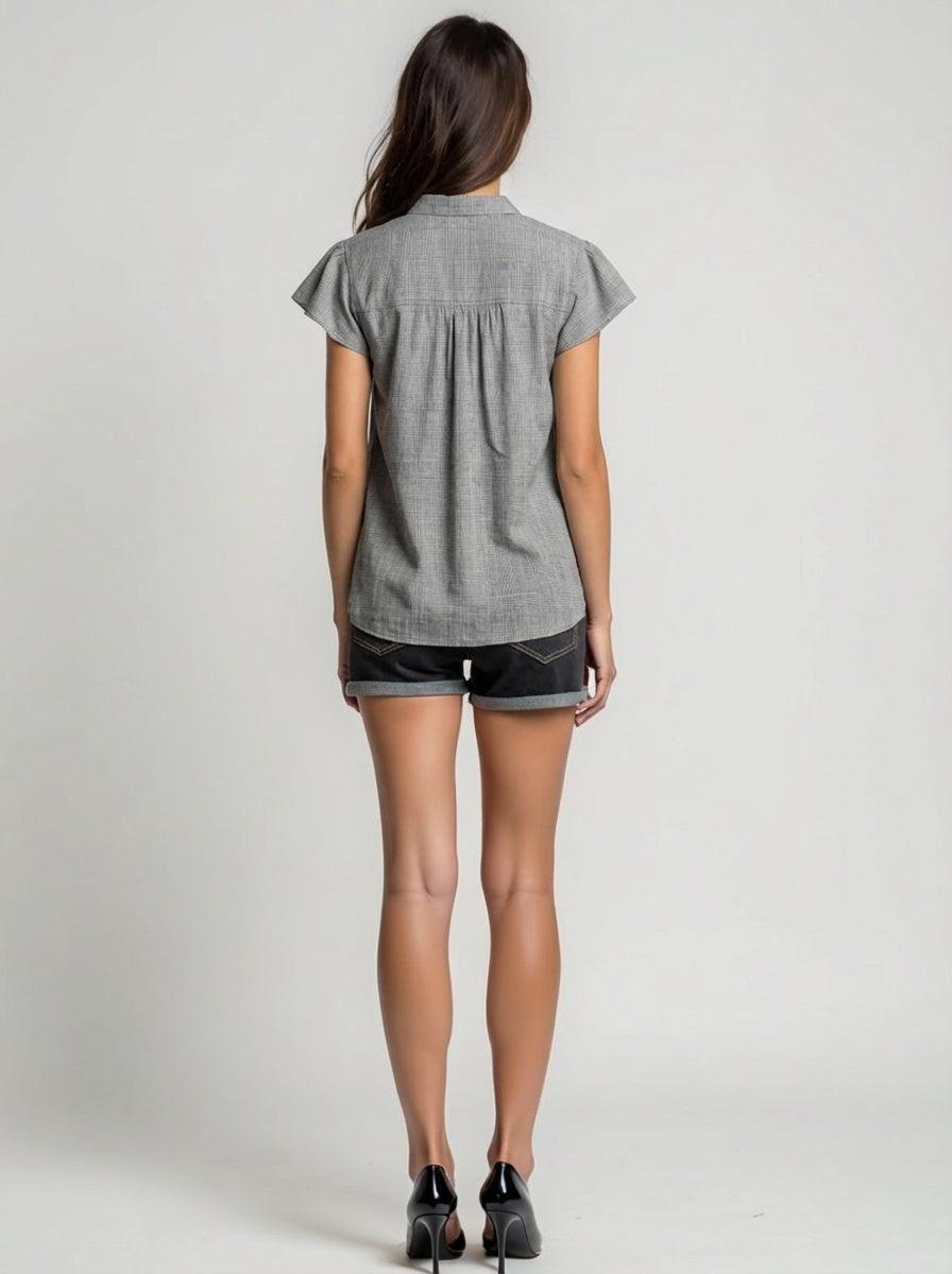 Woman wearing a gray short-sleeve shirt and black shorts on a plain background
