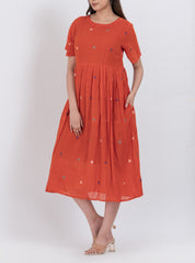  Close-up of the floral embroidery and pleated design on a handwoven cotton dress.