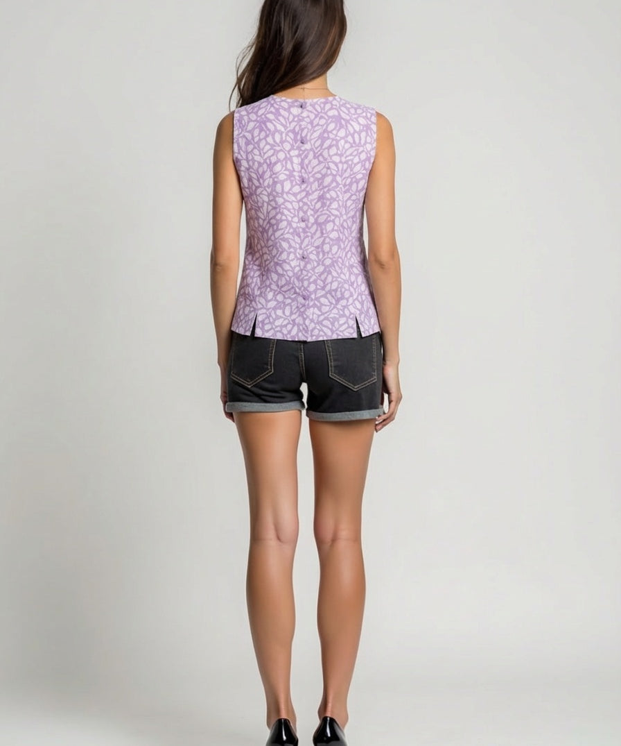 Woman wearing a sleeveless purple floral top and black shorts on a plain background