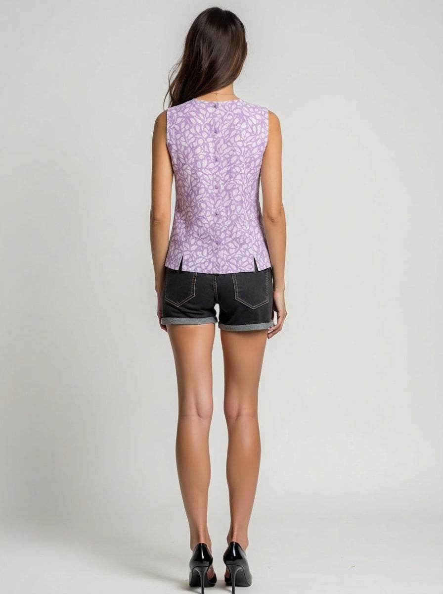Woman wearing a sleeveless purple floral top and black shorts on a plain background