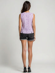 Woman wearing a sleeveless purple floral top and black shorts on a plain background