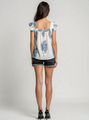 Woman wearing a white blouse with blue floral patterns and black shorts on a plain background