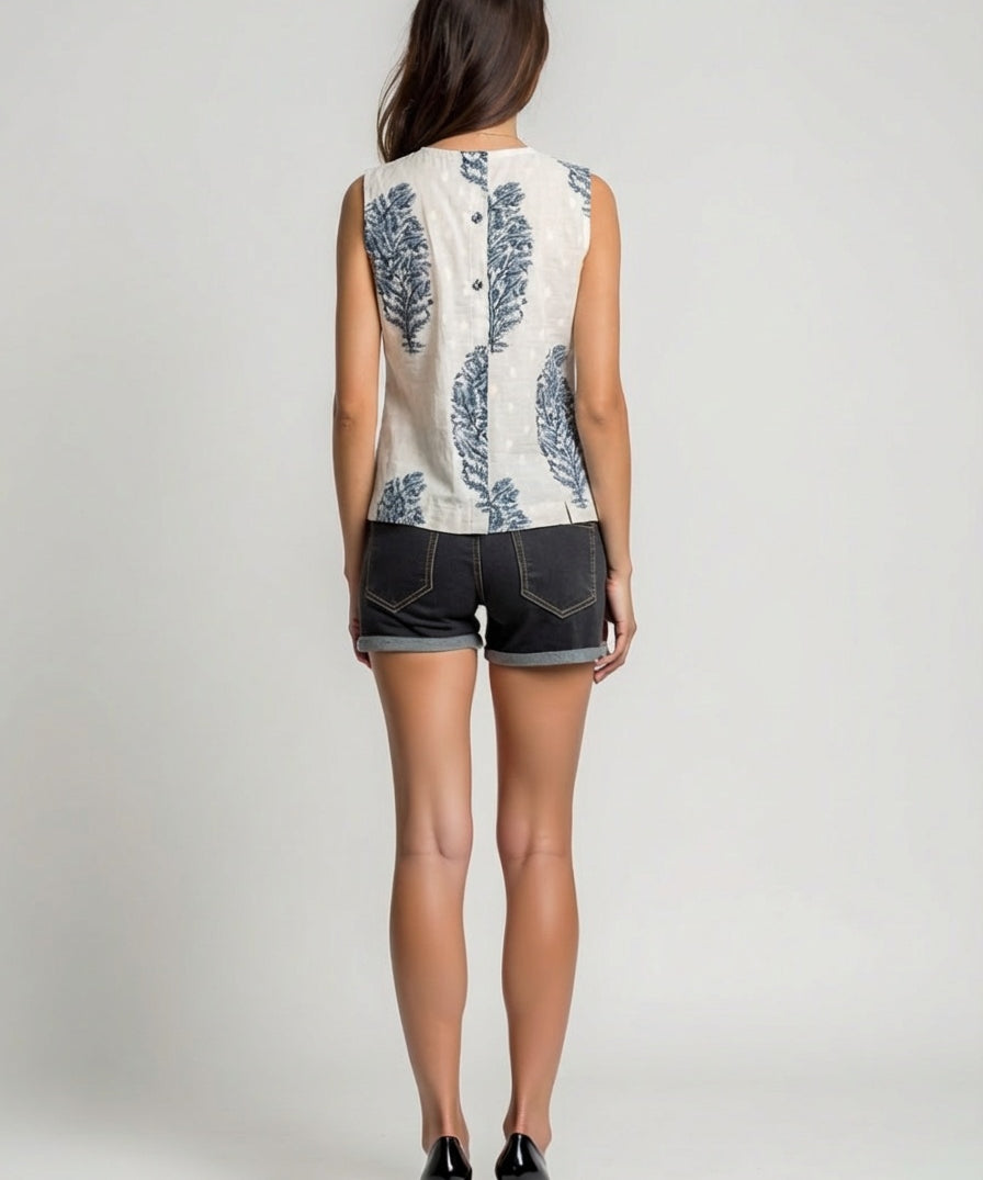 Woman wearing a sleeveless floral top and denim shorts on a plain background