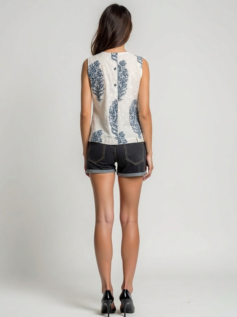 Woman wearing a sleeveless floral top and denim shorts on a plain background