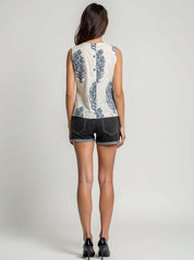 Woman wearing a sleeveless floral top and denim shorts on a plain background