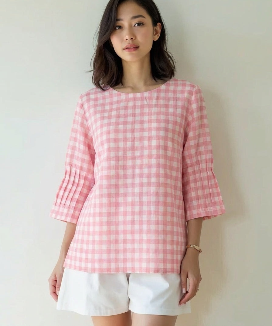 Woman wearing a pink checkered top and white shorts against a plain background