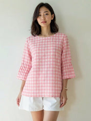 Woman wearing a pink checkered top and white shorts against a plain background