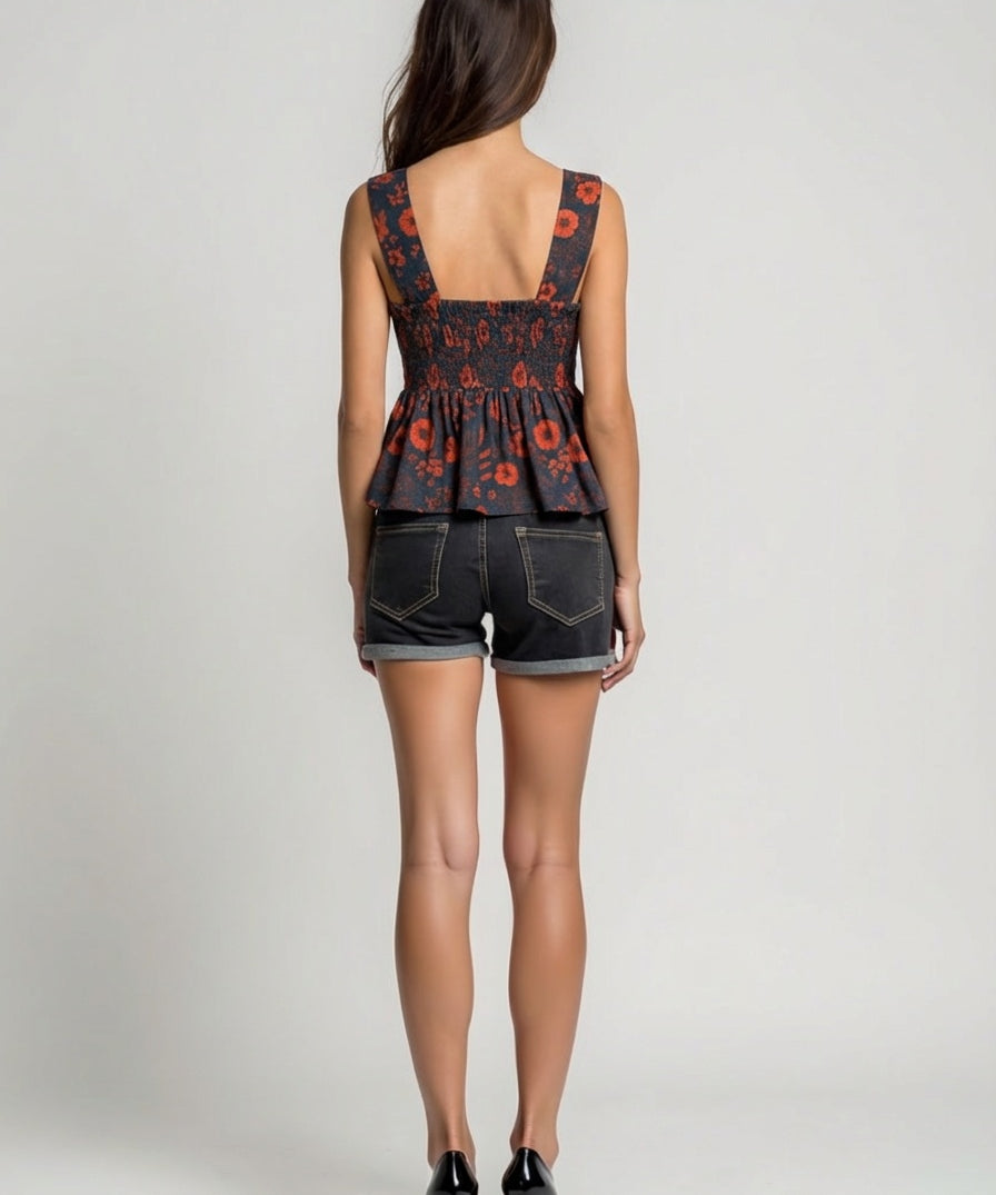 Woman wearing a floral peplum top and denim shorts on a plain background