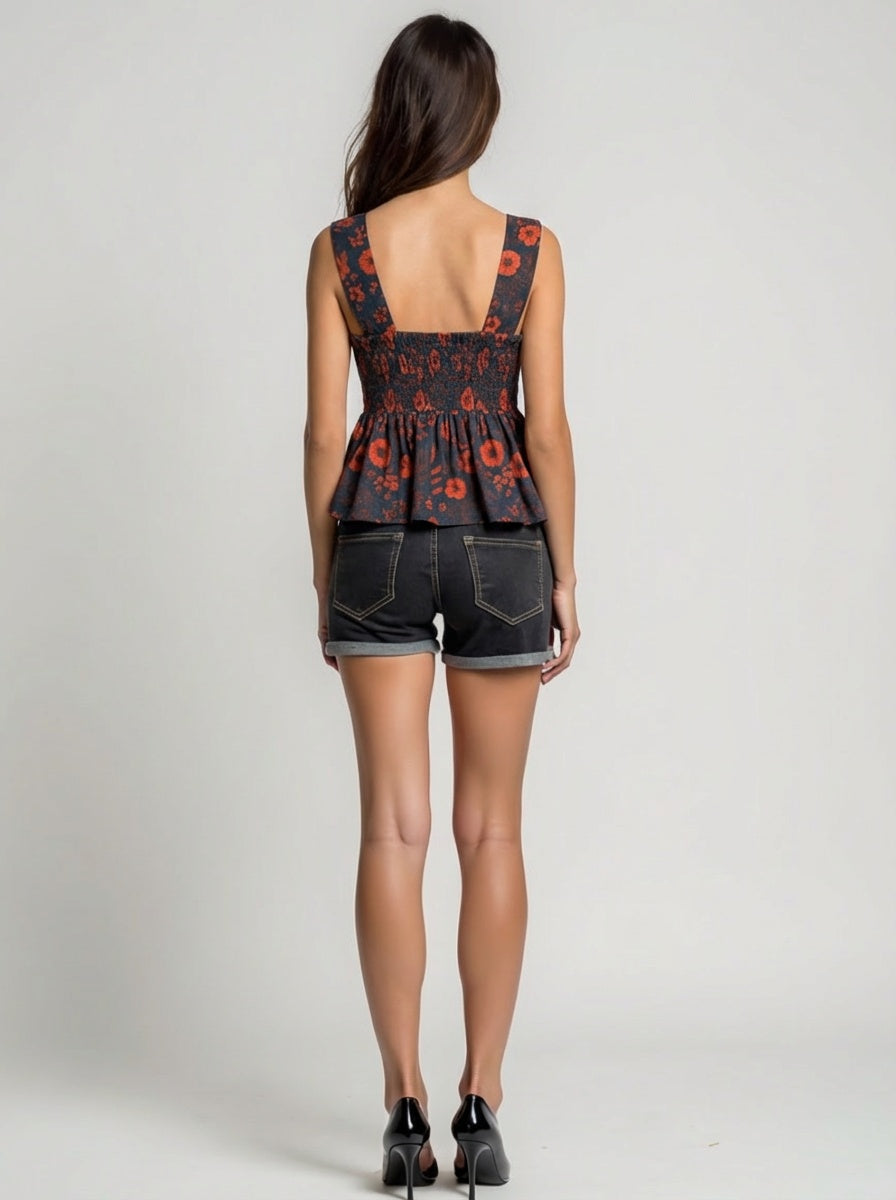 Woman wearing a floral peplum top and denim shorts on a plain background