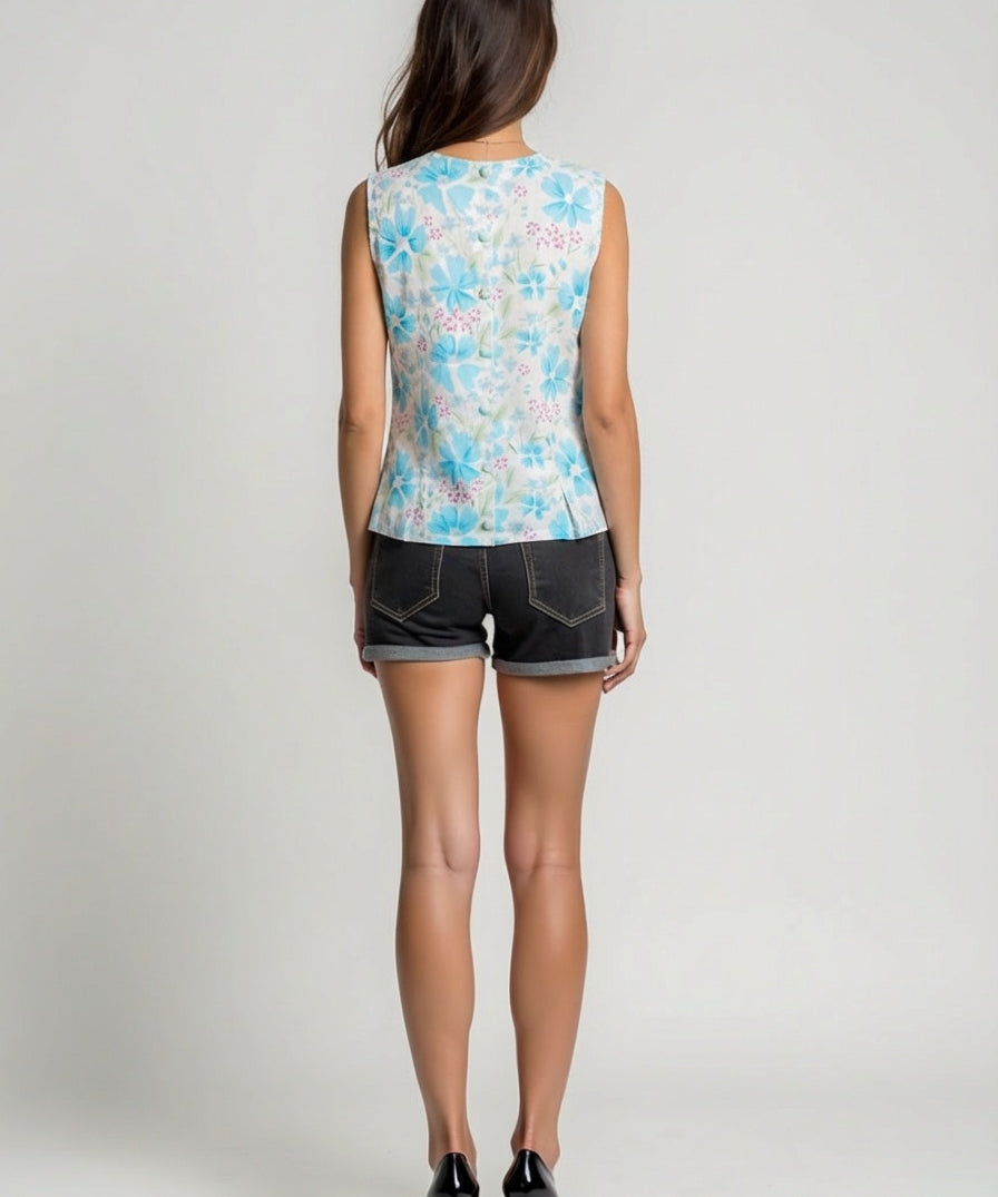 Woman wearing a sleeveless floral top and denim shorts on a plain background