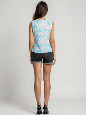 Woman wearing a sleeveless floral top and denim shorts on a plain background