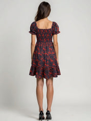 Woman wearing a black dress with red floral pattern on a plain background